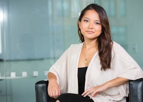A professional Asian businesswoman sitting confidently in a modern office setting.